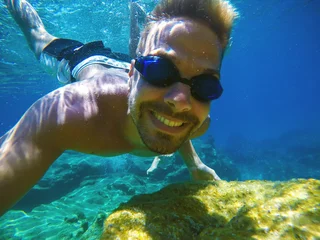 Rolgordijnen Onderwater dichtbij foto van een jonge gelukkig lachende toerist zwemmen in de turquoise zee onder het oppervlak in de buurt van koraalrif voor zomervakantie. © dusanpetkovic1