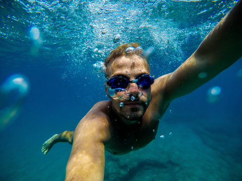 Underwater view of a young adventuristic attractive man swimming and enjoying at the sea for summer holidays while taking a selfie.