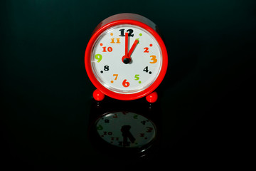 Red alarm clock with time shows 1 o'clock with reflections on an isolated black background.