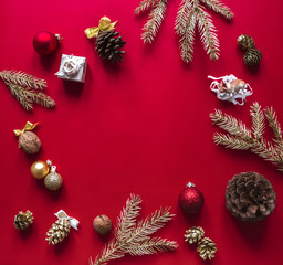 Fototapeta na wymiar On a red raspberry background, the Christmas and New Year decorations and gilded branches of the Christmas tree are arranged in a circle