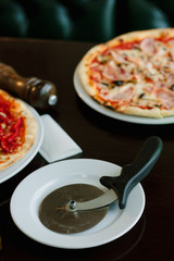 Pizza cutter on white plate. Round knife with pizza on background.