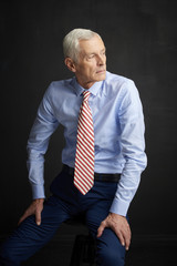 Elderly man portrait. An executive senior man wearing shirt and tie while sitting at isolated black background. 