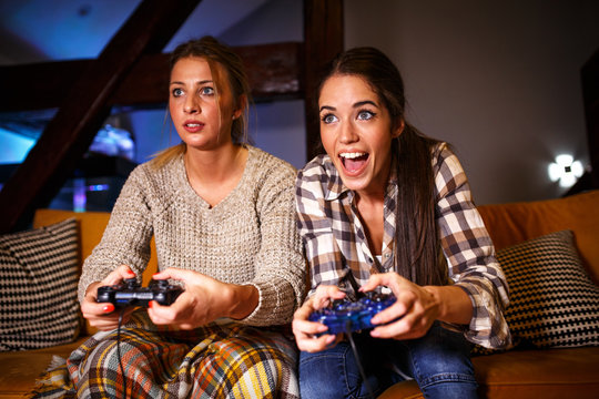Two female best friends sitting at home on pleasant  evening and playing games on console.They challenge each other to win.