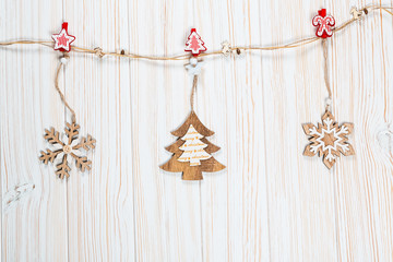 Christmas wooden toys in the form of a Christmas tree and snowflakes weigh on a rope on a white wooden background. Beautiful festive greeting card with free space