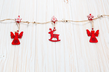 Christmas wooden red toys in the shape of a deer and an angelic rope on a white wooden background. Beautiful festive greeting card with free space