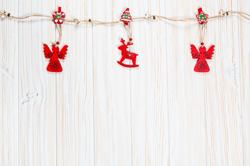 Christmas wooden red toys in the shape of a deer and an angelic rope on a white wooden background. Beautiful festive greeting card with free space
