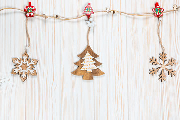Christmas wooden toys in the form of a Christmas tree and snowflakes weigh on a rope on a white wooden background. Beautiful festive greeting card with free space