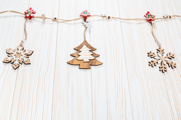 Christmas wooden toys in the form of a Christmas tree and snowflakes weigh on a rope on a white wooden background. Beautiful festive greeting card with free space