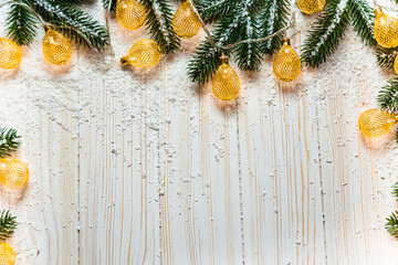 Naklejka na ściany i meble Christmas background with a luminous garland on white wooden table with the branches of the Christmas tree and snow. A beautiful holiday idea for winter postcards and posters. Free space, golden frame