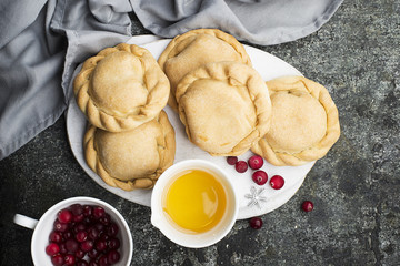 Comfortable food for the whole family. Homemade mini pies made from fresh simple dough with seasonal berries, served with honey. Top view on a gray grunge background.