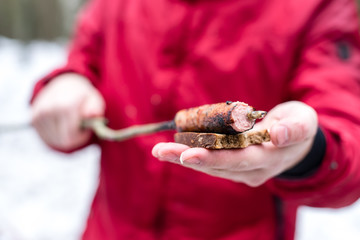 A man in a red jacket holds a fried sausage on a skewer with bread