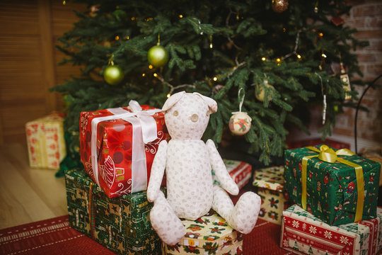 Teddy bear sitting under decorated with lights Christmas tree with gift boxes