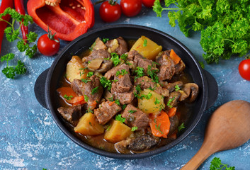 Meat goulash with vegetables, potatoes and mushrooms on concrete, grunge background