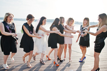 Obraz premium Group of 8 girls wear on black and 2 brides at hen party against sunny beach drinking champagne.