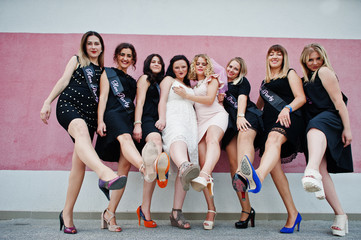 Fototapeta premium Group of 8 girls wear on black and 2 brides at hen party posed against pink wall.
