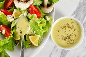 Ceramic bowls with ranch dressing and fresh salad on light background