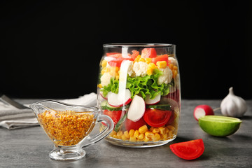 Jar with vegetable salad and mustard sauce in gravy boat on table