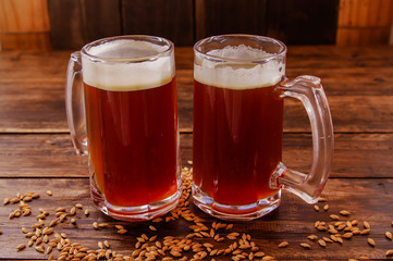 Indoor view of two glasses of beer with wheat in the base on a wooden table in a wooden background