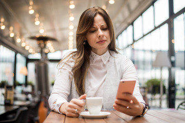 Upset woman reading message on phone in cafe.