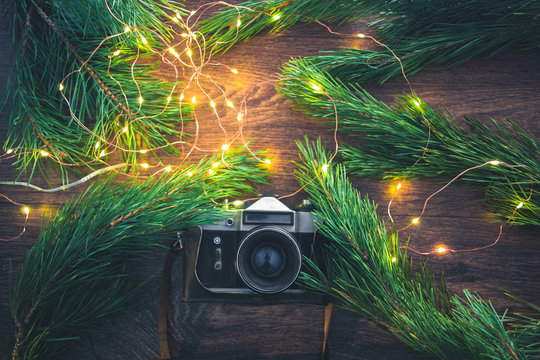 The old camera on a wooden background with Christmas tree branches and lights.