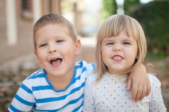 Caucasian brother and sister hugging and making grimace, outdoor portrait