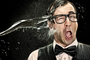 surprised elegant nerd with glasses hit by cold water spray on black background