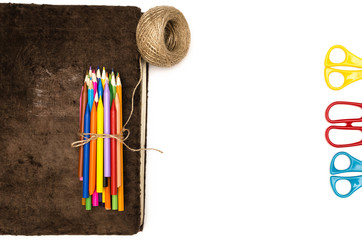 Book and pile of colored pencils tied with a jute rope and scissors isolated on white background....