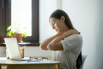 Overwork, sedentary lifestyle concept: millennial businesswoman stretching body, feeling back pain, massaging neck at workplace. Young female manager having rest in home office after finishing her job