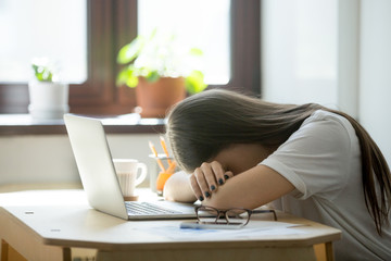 Tired young woman falling asleep at desk after overwork. Exhausted sleep deprived stressed female manager lying on table and sleeping after hard working day, no energy left - obrazy, fototapety, plakaty