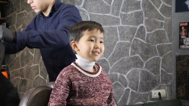 Barber covering the Asian child with a cloak, the child laughing 60 fps