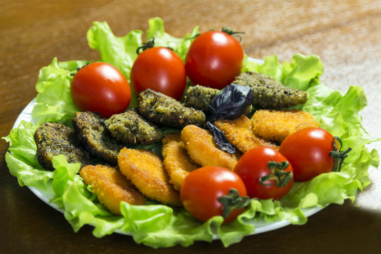 Tasty meat or fish nagets in a plate on green lettuce leaves decorated with tomatoes. Close-up.