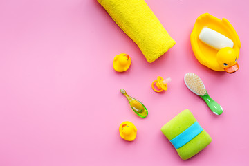 Bath accessories for kids. Yellow rubber duck, soap, sponge, brushes, towel on pink background top view copyspace