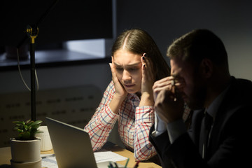 Depressed unhappy businessman and businesswoman having night shift in office and worried about work problem. Overwork, deadline, bankrupt work concept.