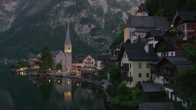Wide panning shot of church at lake waterfront at night / Hallstatt, Austria