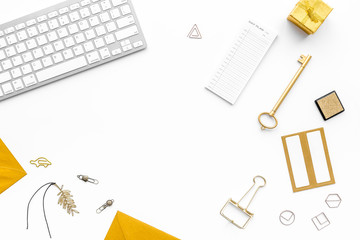 Fashoin in the workplace. Office desk in a trendy gold color. Stationery near keyboard on white background top view copyspace