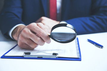 Businessman checking a document with a magnifying glass