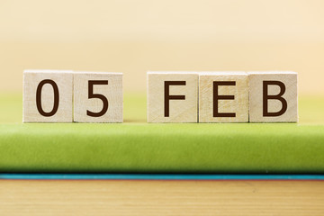 Wooden cube shape calendar for FEB 5 on green book, table.  