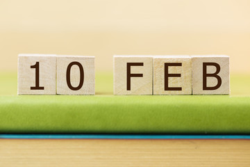 Wooden cube shape calendar for FEB 10 on green book, table. 