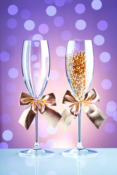 Festive champagne glasses with golden bows and beads on a glass table with a beautiful blue bokeh