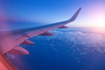 View from passenger's seat in airplane flying above clouds in dramatic sunset light.