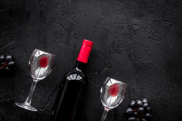 Taste red wine. Bottle of red wine, glass and black grape on black stone background top view copyspace