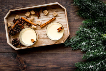 Winter attributes. Glasses of classic eggnog with spices near spruce branch on dark wooden background top view