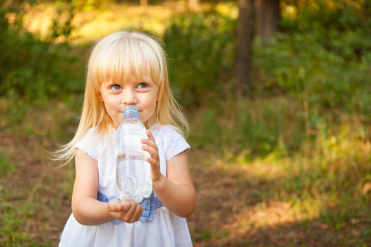 Cute little girl drink water from bottle outdoors