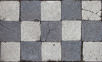 Old mosaic gray and white tile on a floor, in a chess arrangement of colors. Some squares are...