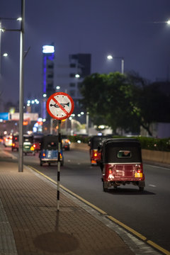 A lot of three-wheeled tuk-tuk and other transport pass by the road sign "No signal" on the street on the way to the city.