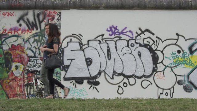 Wide shot of couple walking near wall with graffiti / Berlin, Germany