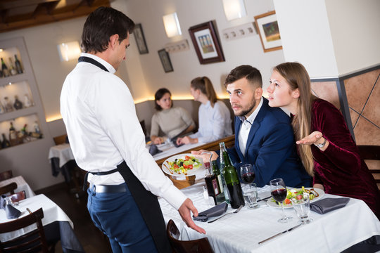 Dissatisfied family couple talking to apologetic waiter