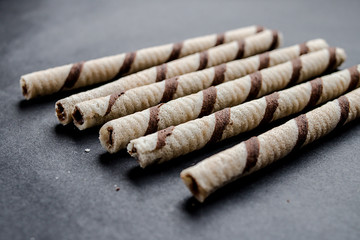 Waffle rolls with chocolate on dark background, close up