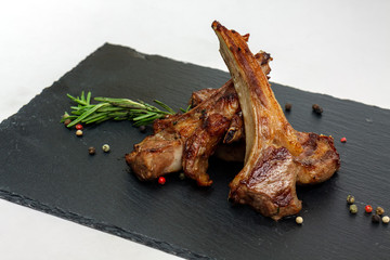 Roasted lamb ribs with rosemary and pepper on the black plate. Background is white