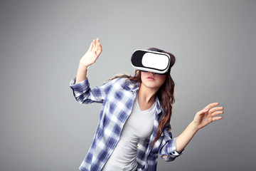Young girl in virtual reality goggles on grey background